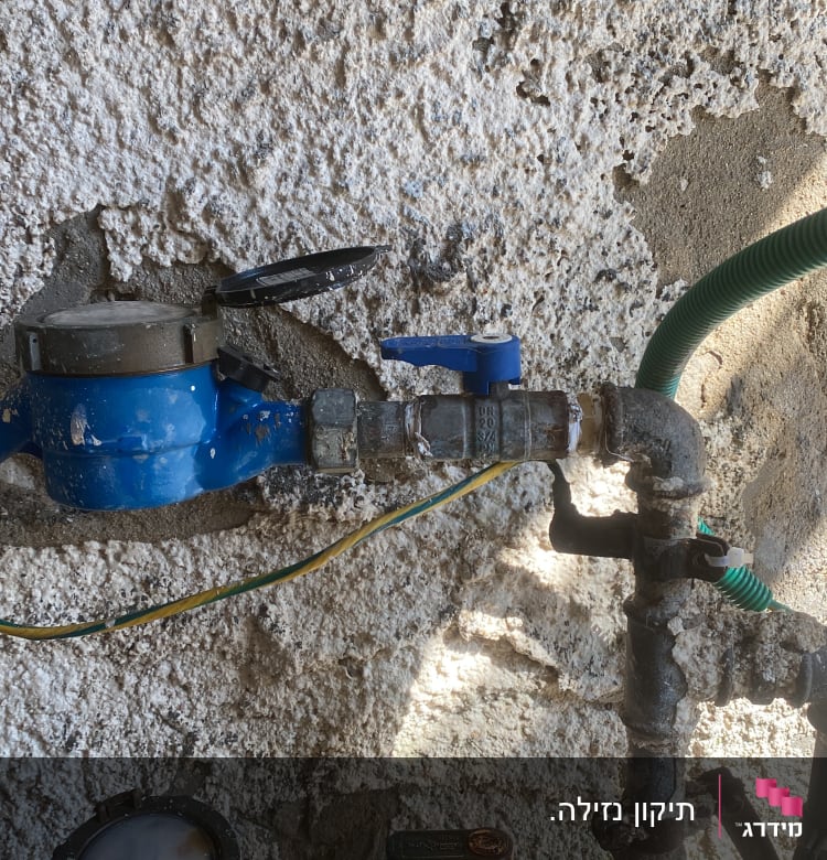 מד מים כחול עם צינורות וברזים על קיר